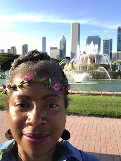 Black woman in a rose and leaf headband in in front of the Buckingham Fountain and Chicago Skyline