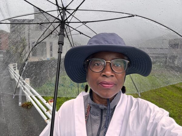 Woman in a while pilgrims coat under an umbrella.